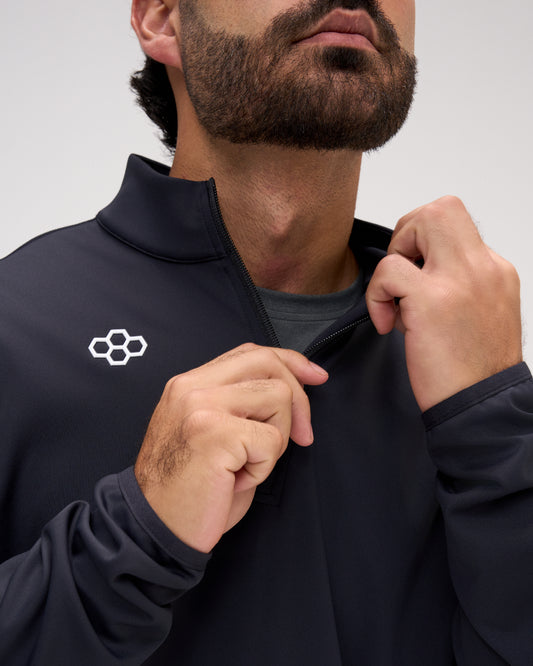 Close-up of a man wearing a black athletic zip-up jacket with a white geometric logo on the chest, adjusting the collar.
