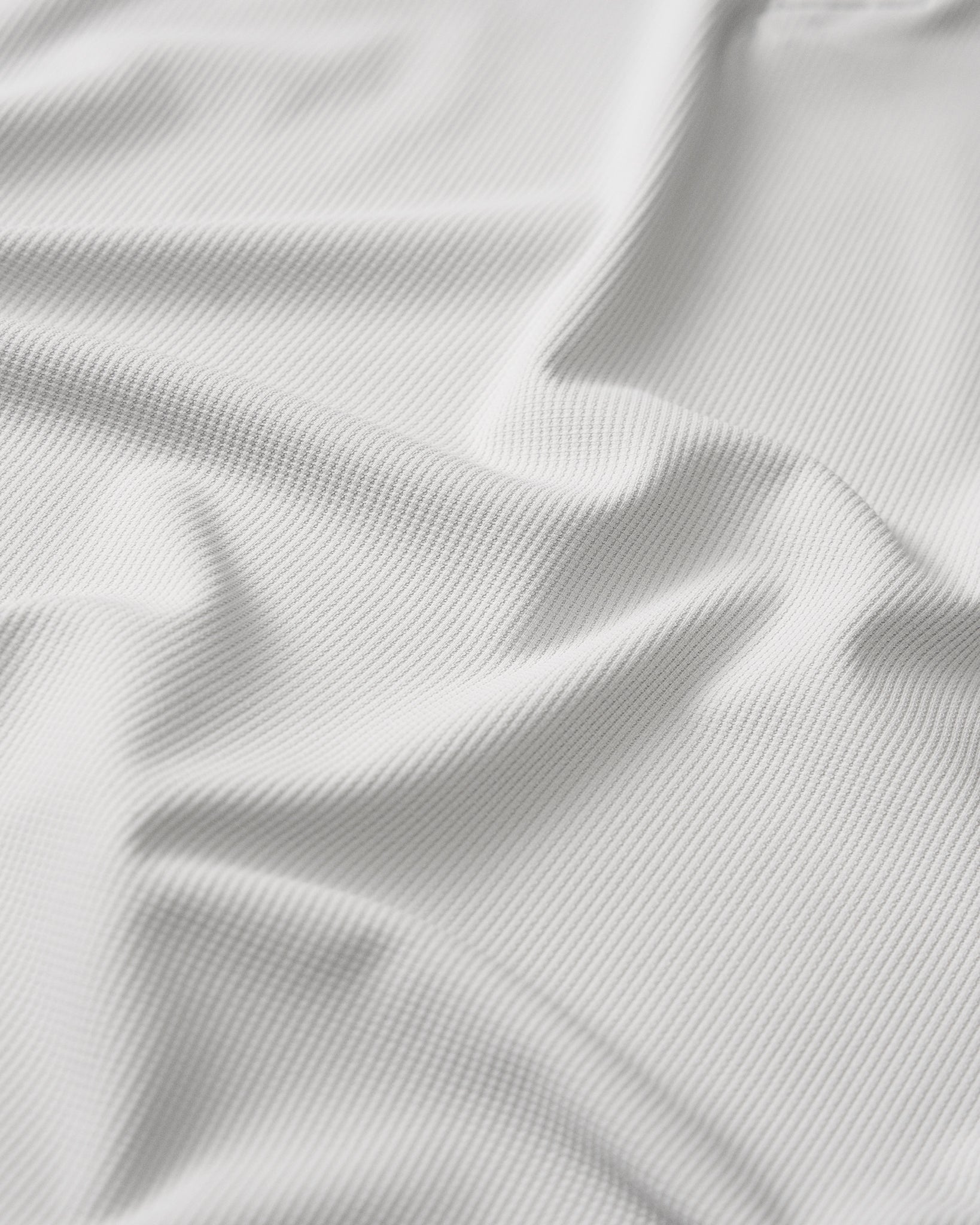Close-up detail of the RUDIS Go-To Polo in Lunar Gray, highlighting the finely ribbed, textured fabric with subtle vertical lines and natural folds that showcase the material's surface and construction.