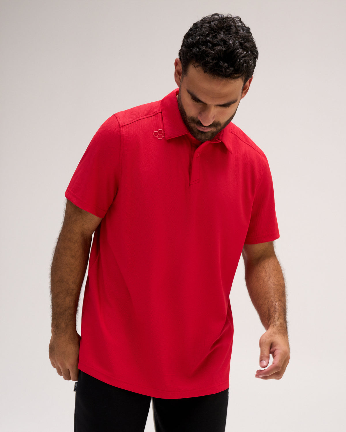 Male model wearing the RUDIS Go-To Polo in Red, showcasing the front design with a classic polo collar, button placket, short sleeves, and subtle RUDIS emblem near the shoulder.