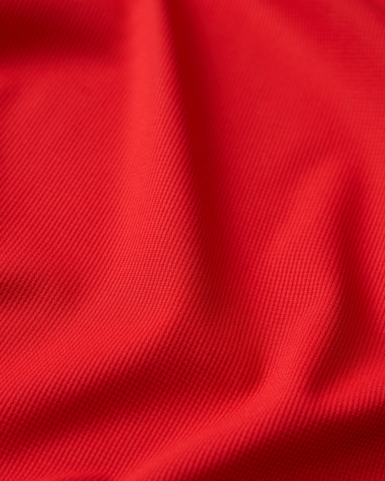 Close-up detail of the RUDIS Go-To Polo in Red, highlighting the finely ribbed, textured fabric with subtle diagonal lines and natural folds that showcase the material's surface and construction.
