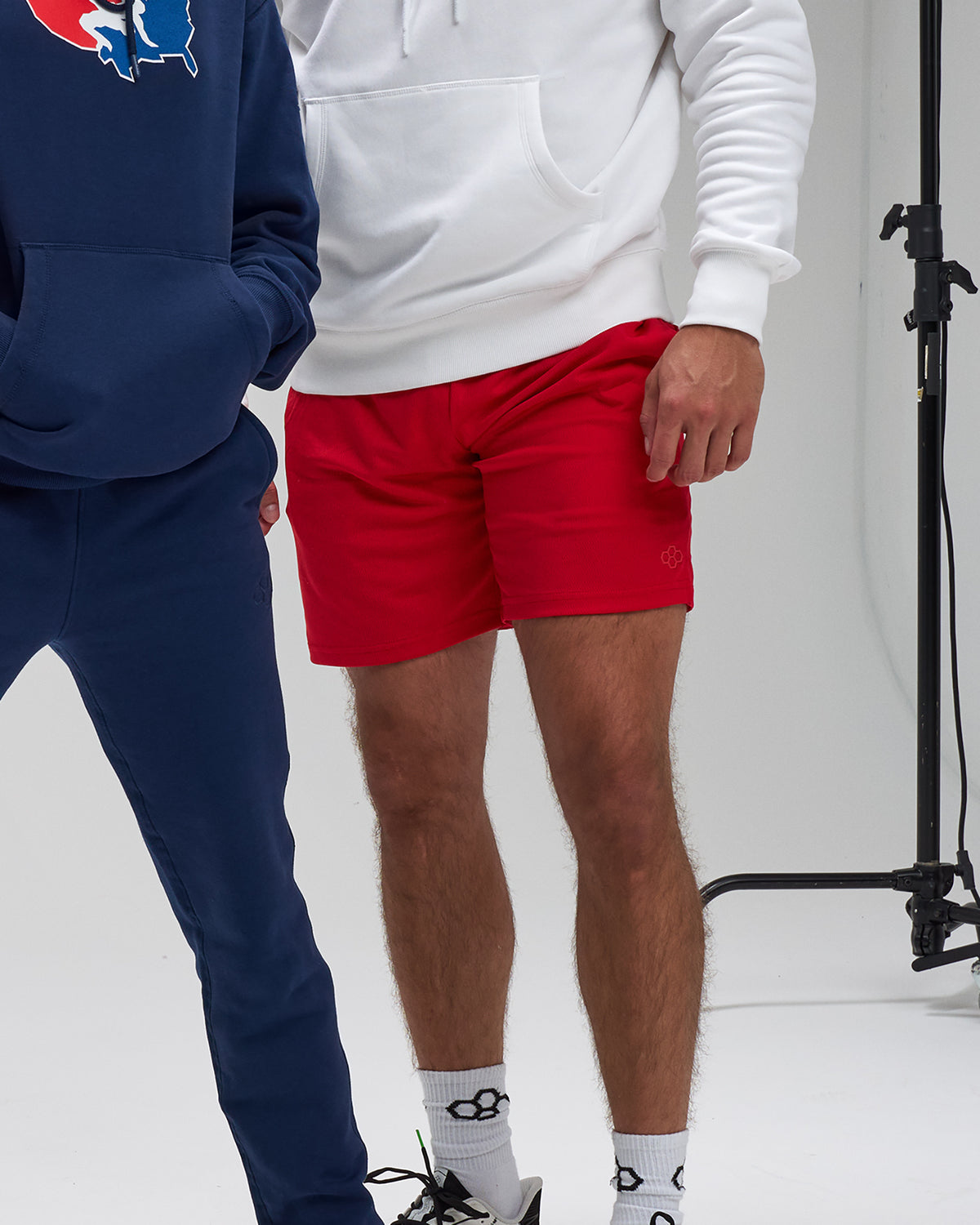 Two people wearing hoodies and shorts in a studio setting.