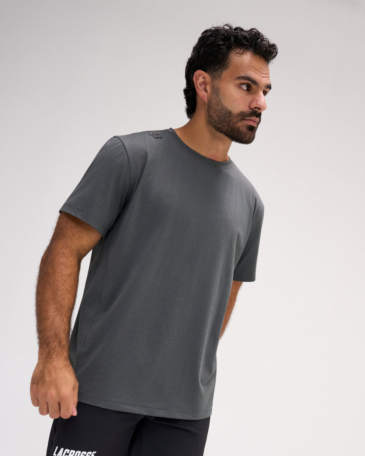 Model wearing the RUDIS Performance Heather T-Shirt in Heather Carbon, featuring medium-gray heathered fabric, short sleeves, a crew neckline, and subtle RUDIS shoulder branding.
