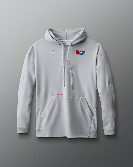 A light gray pullover hoodie displayed against a red-to-blue gradient background. The hoodie features a front kangaroo pocket, ribbed cuffs, and a drawstring hood. On the upper left chest, there's a small white hexagonal RUDIS logo. On the right chest, a red, white, and blue USA Wrestling logo shows a wrestler in action over a map of the United States. Below the pocket, centered on the lower torso, is small text reading "USA WRESTLING" in black and red font.