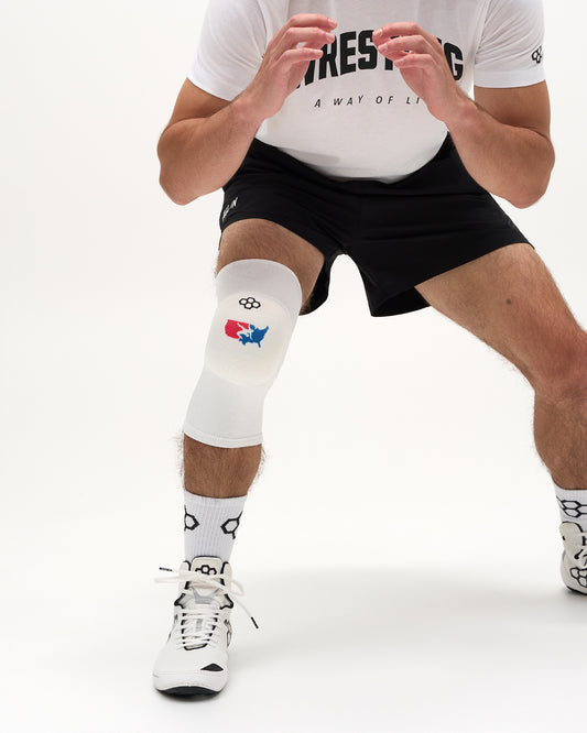 RUDIS USA Wrestling Map Cushion Knee Pad in white worn by a wrestler in a low wrestling stance.