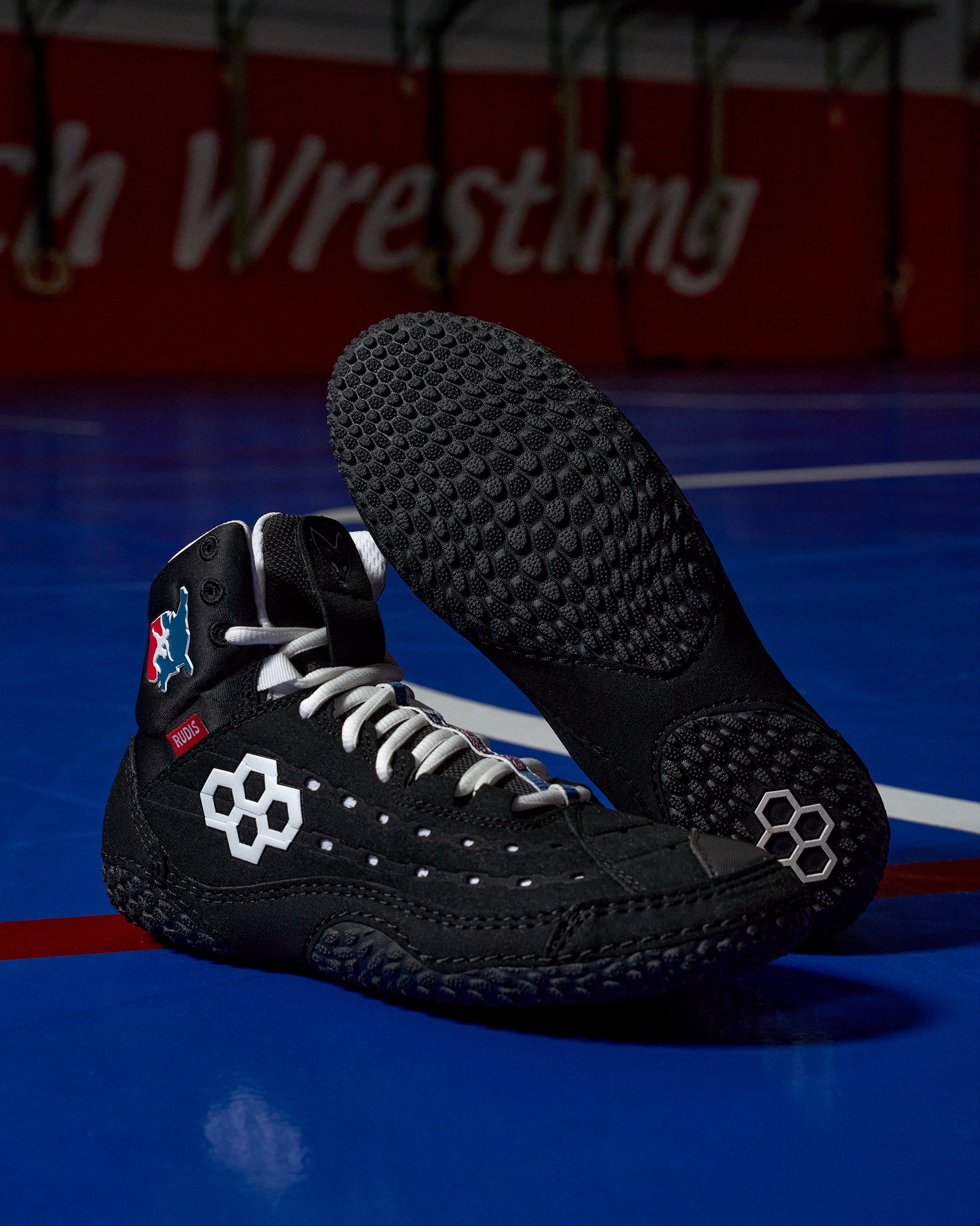 Black wrestling shoes with white accents on a blue mat background
