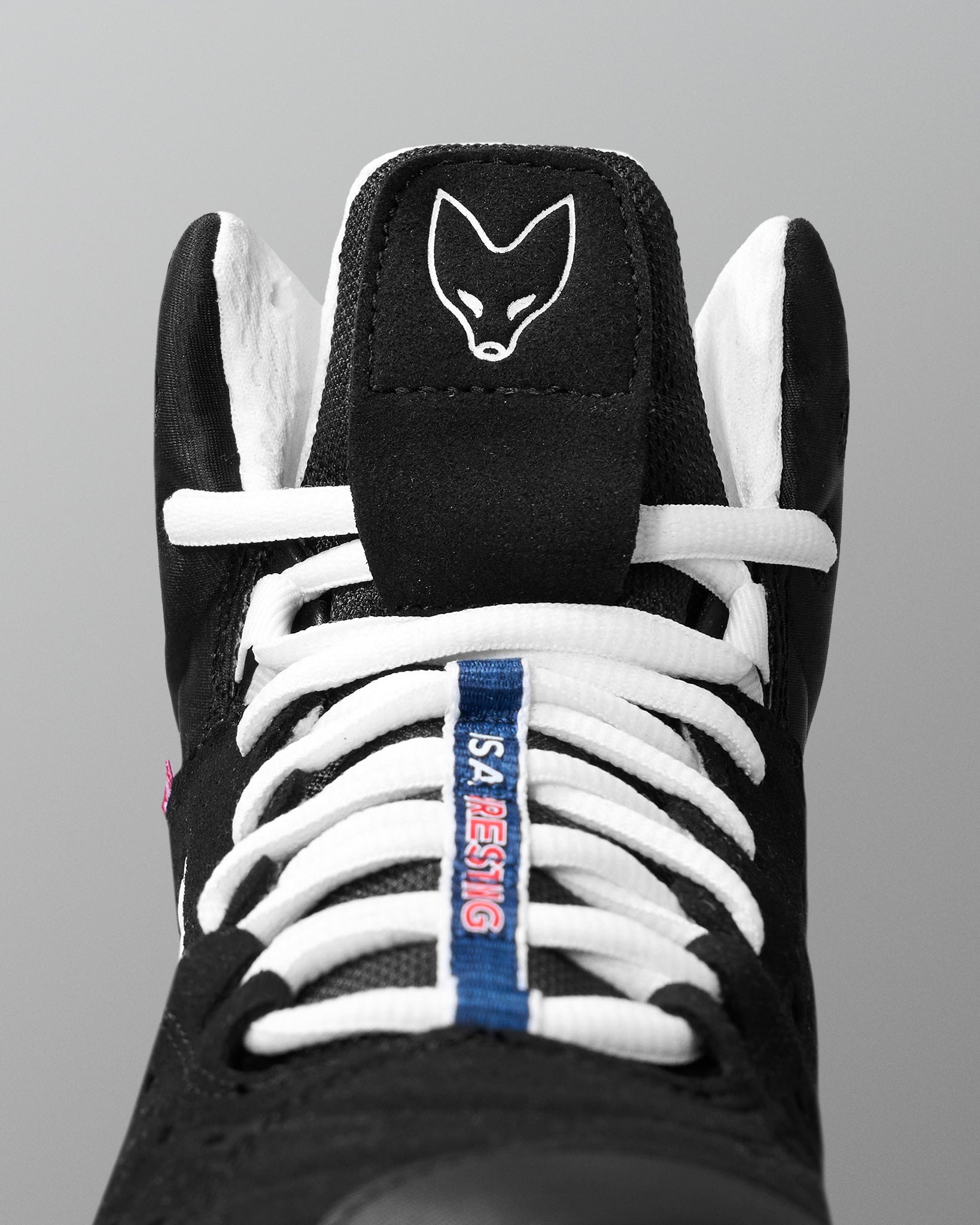 Black wrestling shoe with white laces and a logo on a gray background