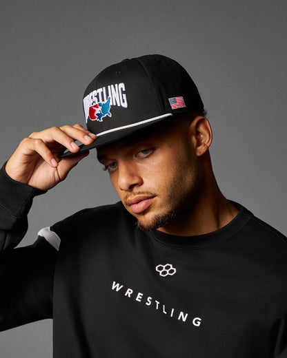 Man wearing a black cap and black 'Wrestling' sweatshirt on a gray background