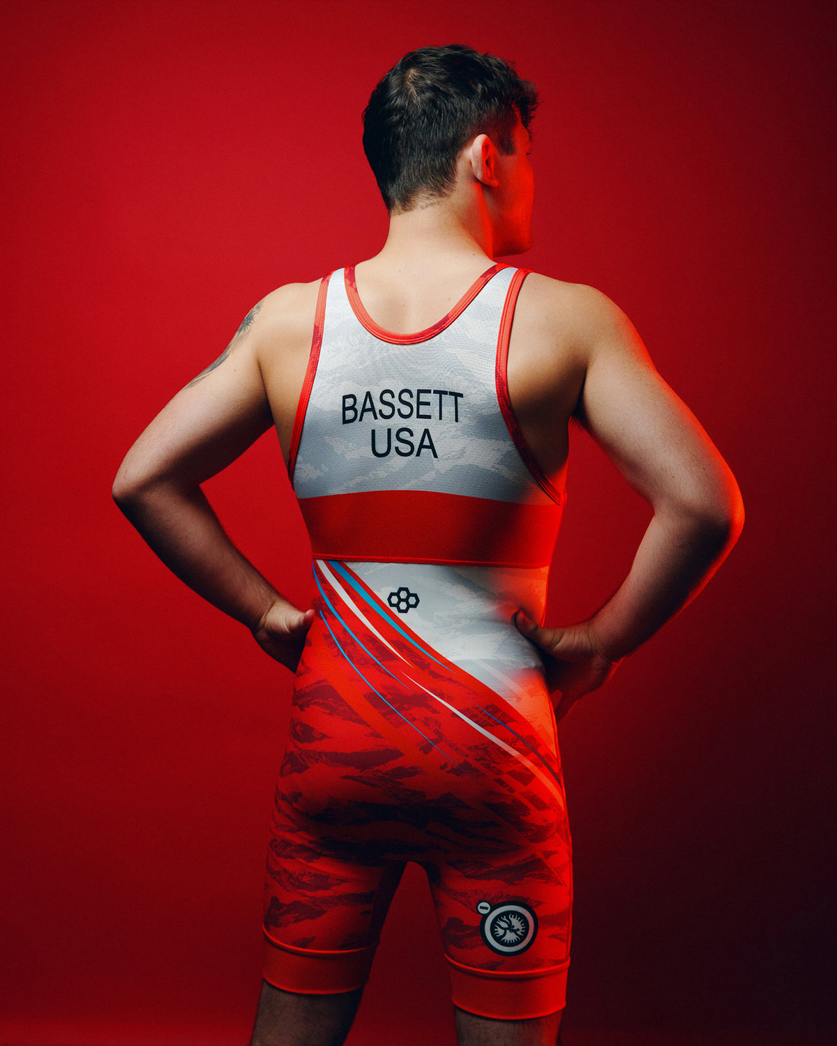 Wrestler modeling the back of the RUDIS USA Wrestling Shooting Star Elite 2.0 Singlet in red, featuring BASSETT USA lettering, diagonal stripes, and red leg bands.