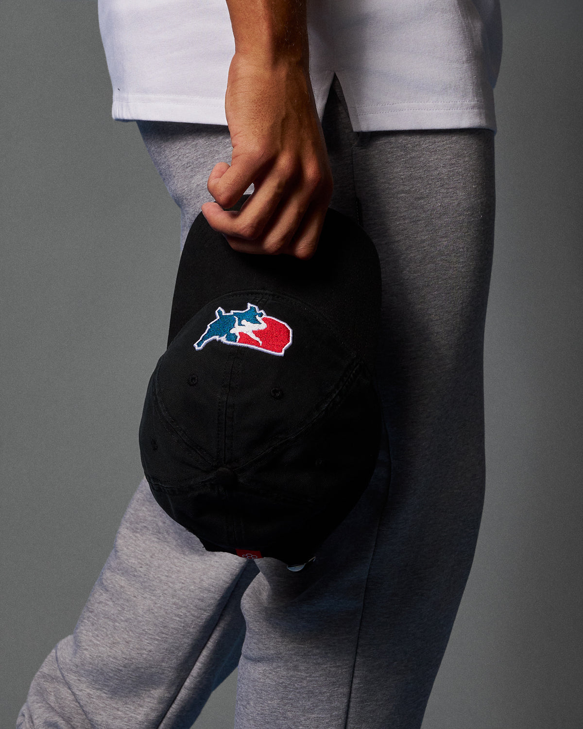 Person holding a black cap with a logo against a gray background