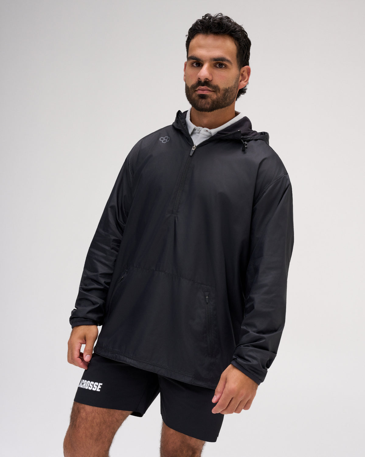 Front three-quarter view of a male model wearing the RUDIS Motion Windbreaker in Black, featuring a quarter-zip front, adjustable hood, long sleeves, zippered pockets, and subtle RUDIS shoulder branding.