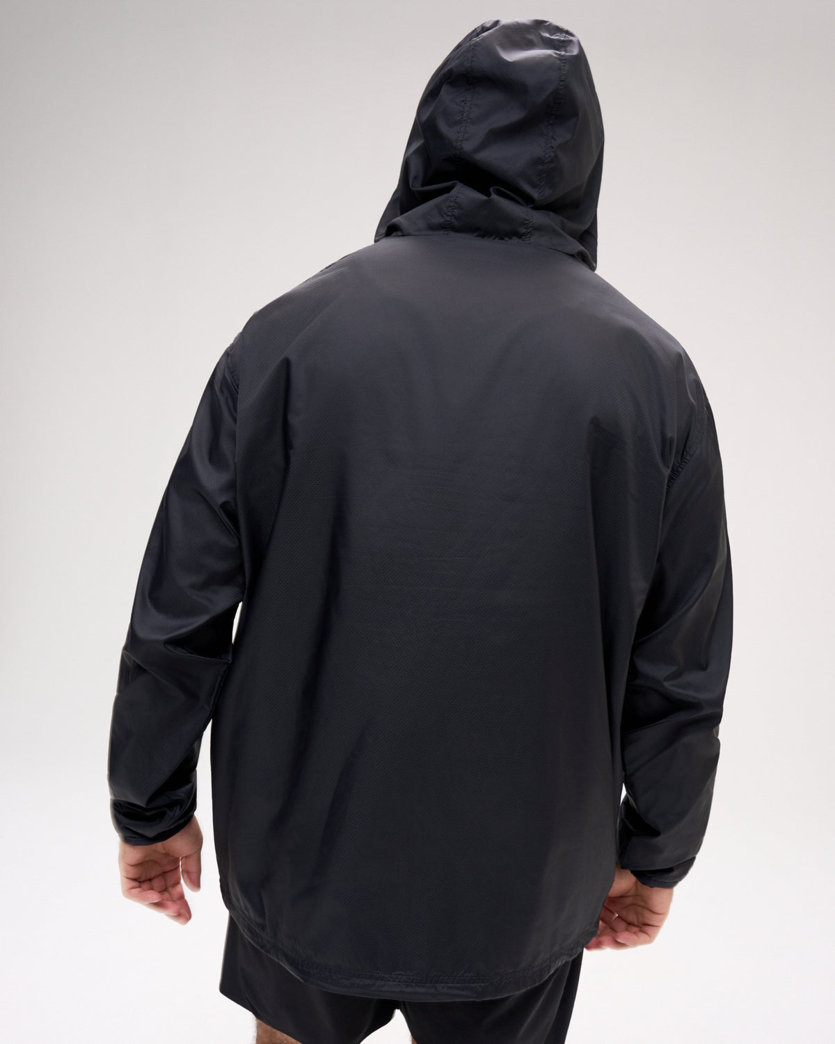 Rear view of a male model wearing the RUDIS Motion Windbreaker in Black with the hood up, showcasing its streamlined silhouette, full-length sleeves, and clean, minimalist back design.