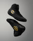 Black high-top wrestling shoes with gold Batman logo and honeycomb pattern accents, shown from multiple angles on a gray gradient background.