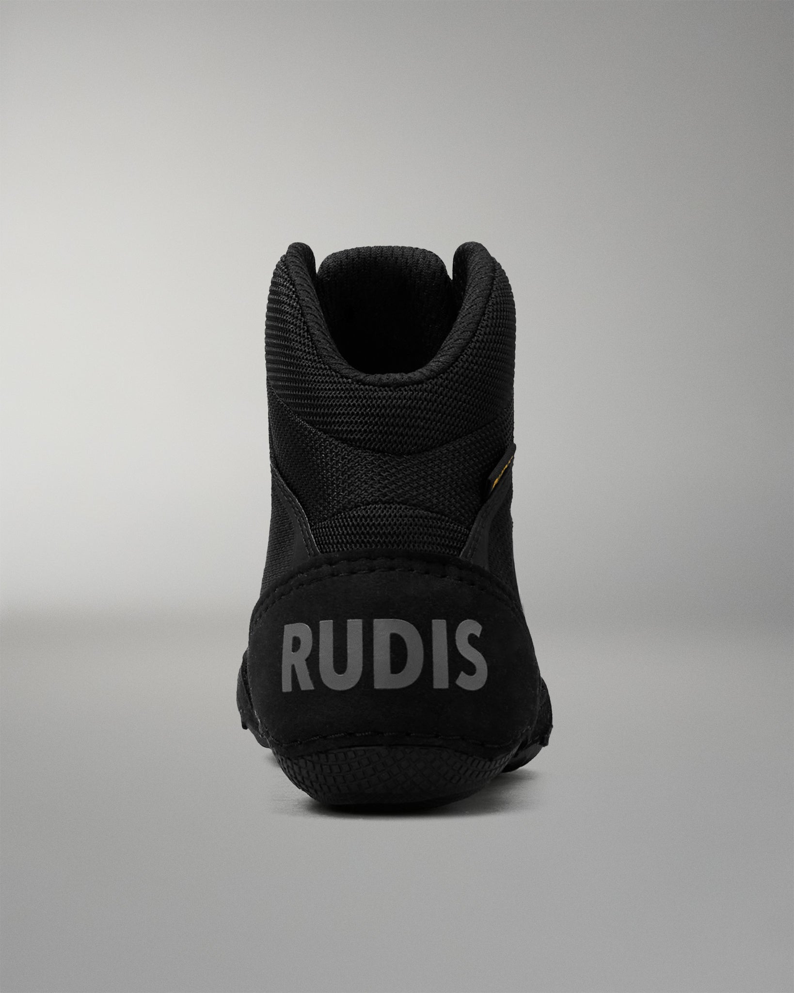 A black high-top wrestling shoe shown from the back, featuring the brand name 'RUDIS' in light gray text on the heel, set against a neutral gray background.