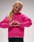 Young girl wearing a pink hoodie with a heart shape made by her hands on a gray background