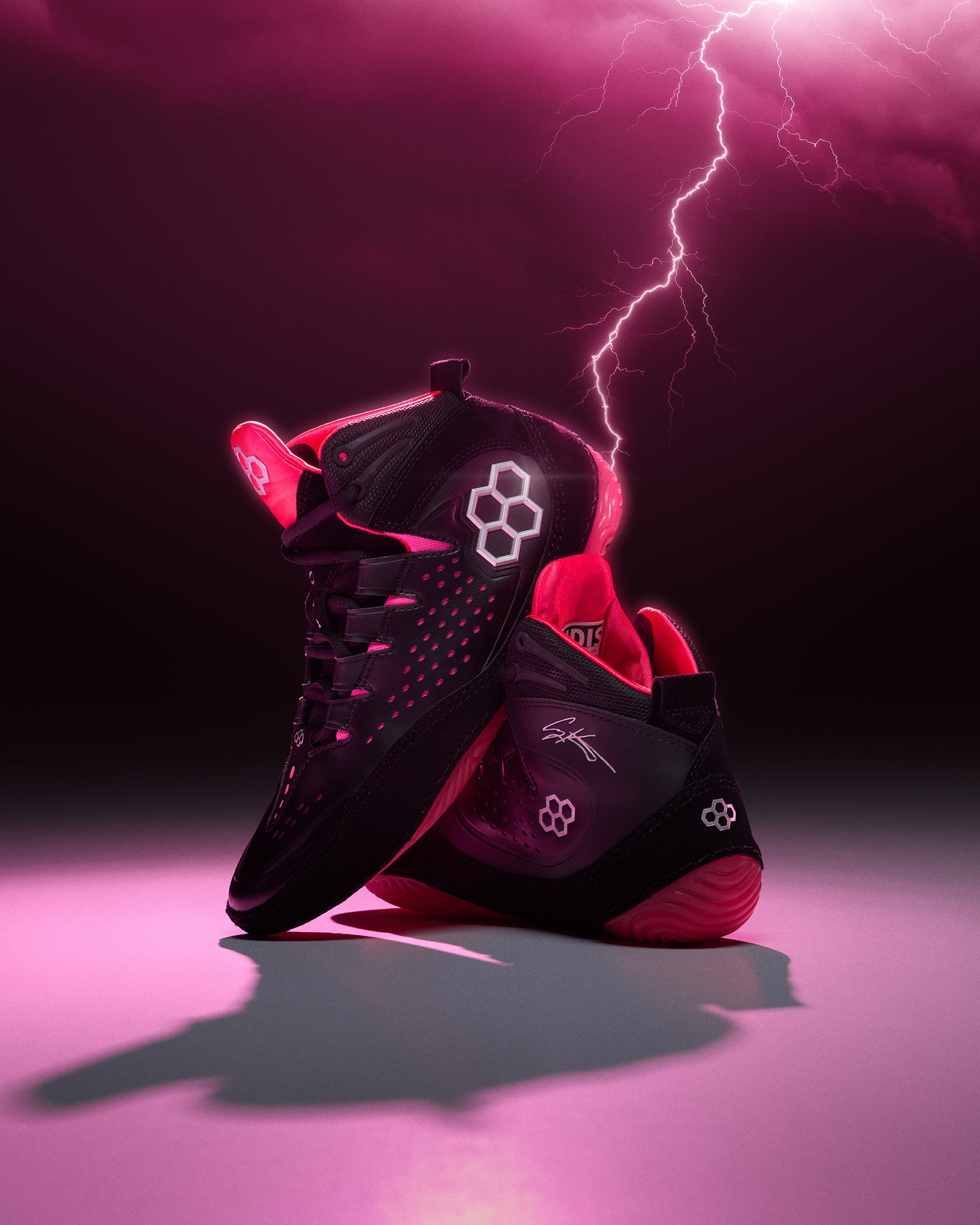 Black and pink wrestling shoes with a lightning bolt effect on a dark background