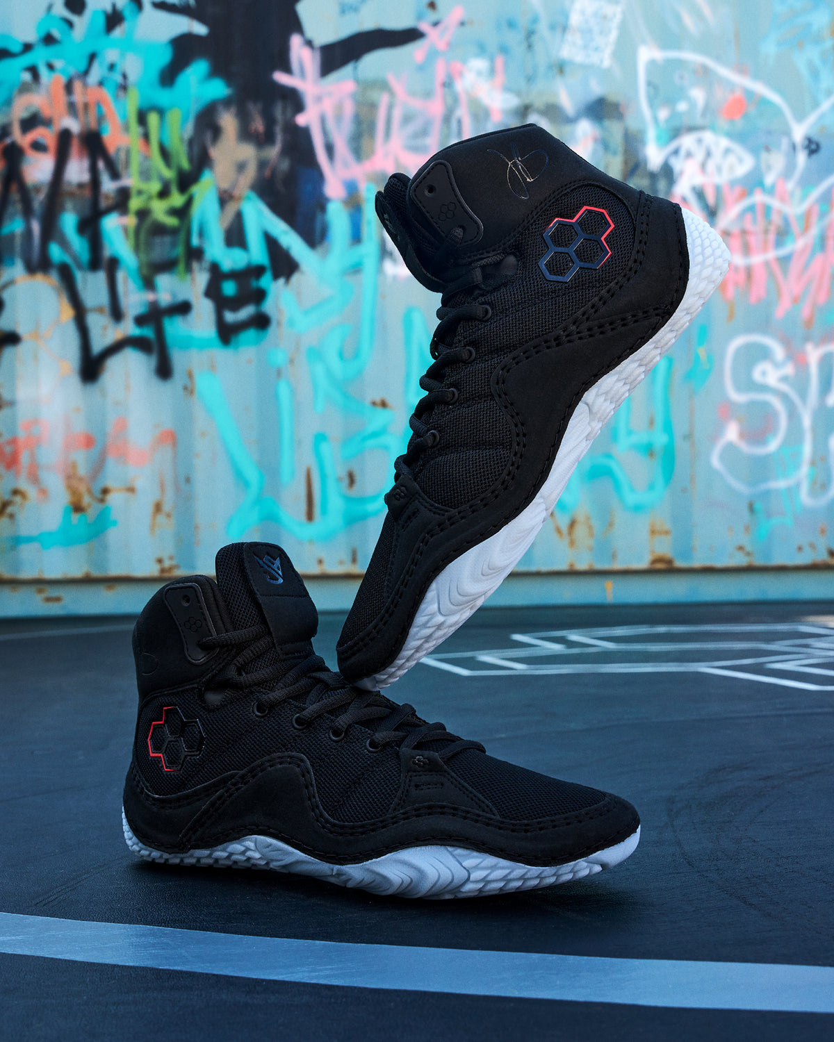 RUDIS JB1 Youth Wrestling Shoes in Dark Shark displayed on a wrestling mat, showcasing the black high-top design, RUDIS branding, red accents, and light blue wrestling outsole.