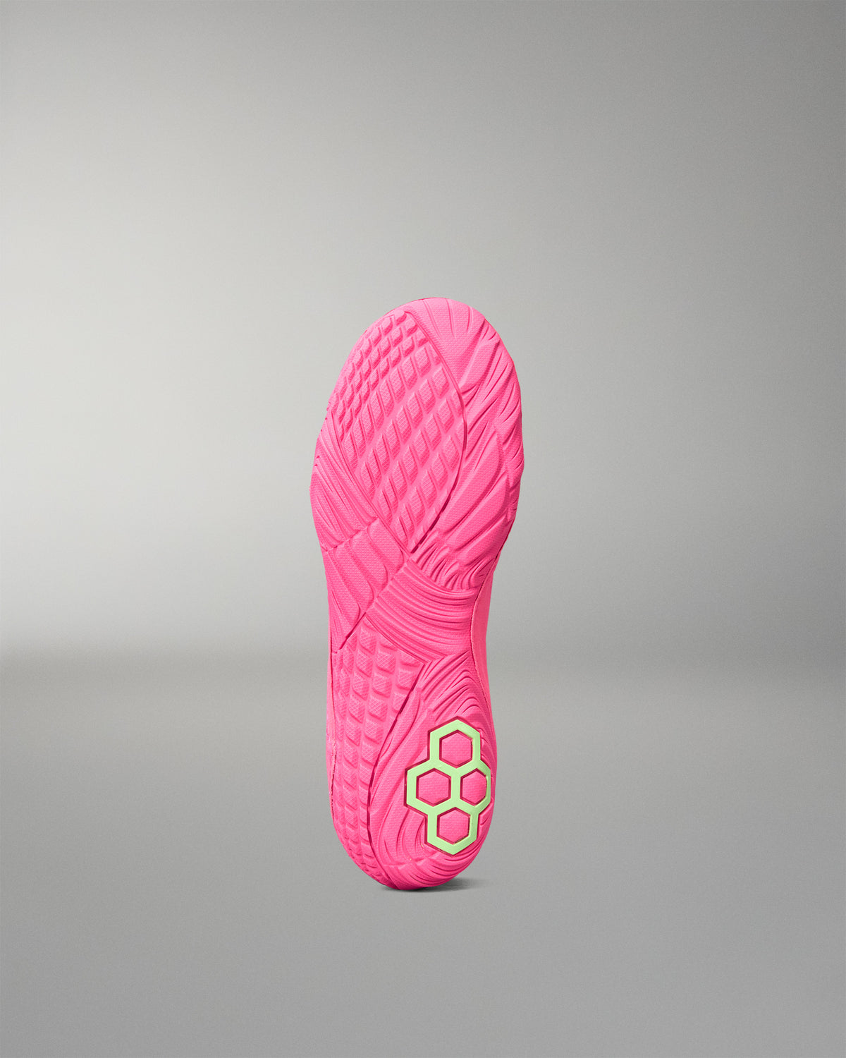 A bright pink wrestling shoe sole shown upright against a neutral gray gradient background, featuring a textured tread pattern and a small neon yellow-green geometric logo near the heel.