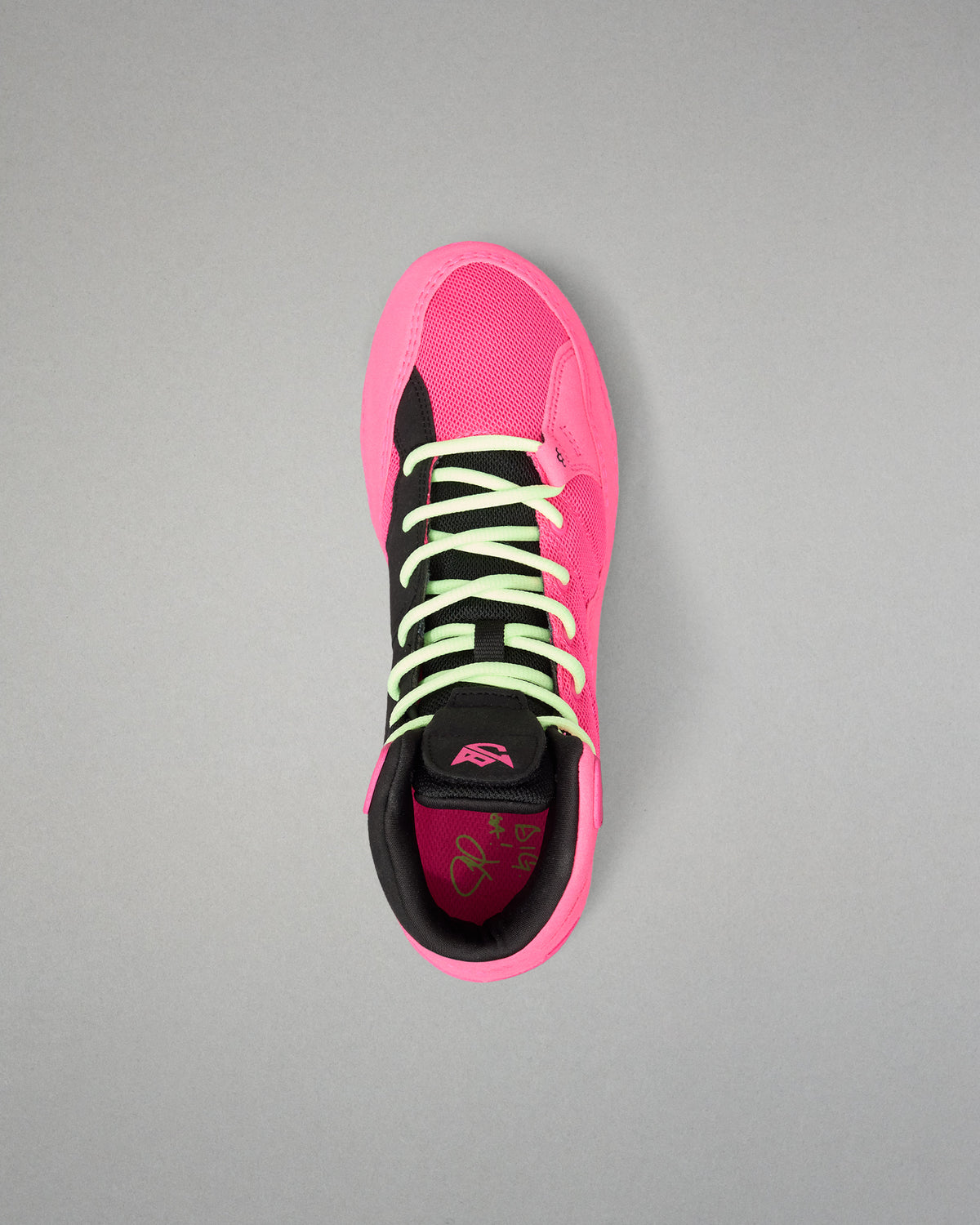 A single high-top wrestling shoe shown from a top-down view on a neutral gray background. The shoe features a vibrant hot pink upper and sole, black overlays, neon yellow-green laces, and a black collar.