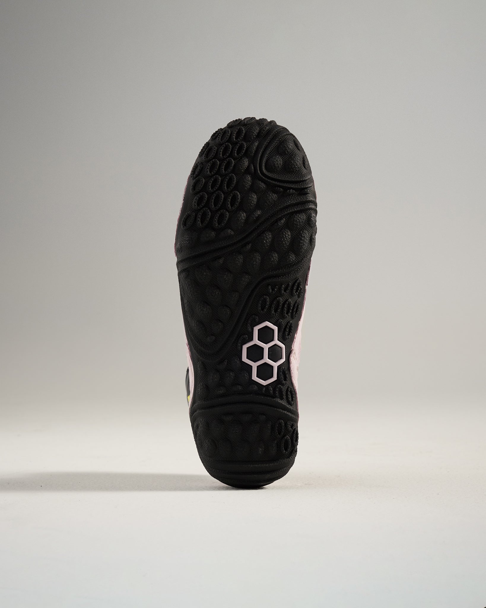 A close-up view of the textured black sole of a sneaker featuring a pink accent and a modern design