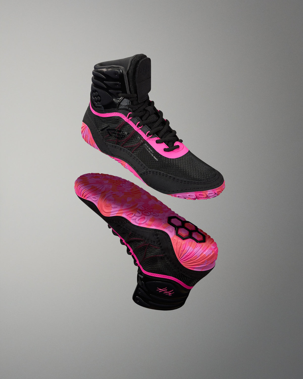 A pair of high-top athletic Wrestling shoes shown floating against a neutral gray gradient background. The shoes are primarily black with vibrant hot pink accents on the laces, side details, and outsole, featuring a distinctive pink and black patterned sole.