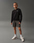 A young boy stands confidently in a black sweatshirt and gray shorts wearing white sneakers and patterned socks against a minimalist gray background