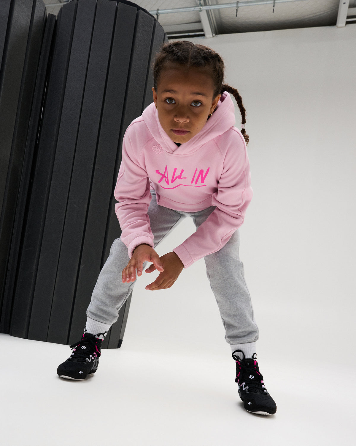 RUDIS All In Youth Tech Fleece Hoodie in Pink shown in an athletic stance, highlighting the youth fit, All In chest graphic, hood, and performance-inspired RUDIS styling.
