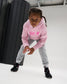 RUDIS All In Youth Tech Fleece Hoodie in Pink shown in an athletic stance, highlighting the youth fit, All In chest graphic, hood, and performance-inspired RUDIS styling.