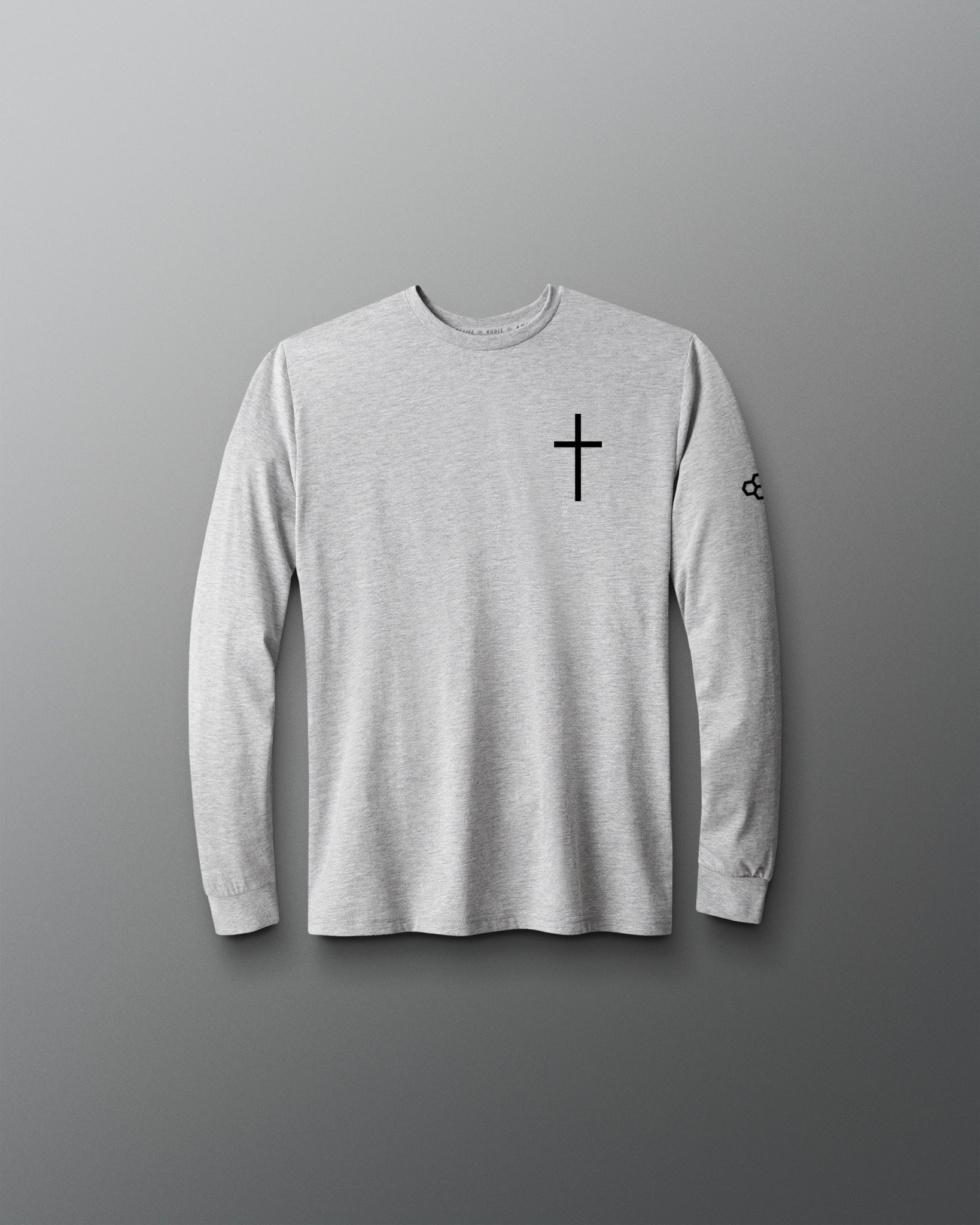 A light gray long-sleeve crewneck shirt with a black cross printed on the left chest and a small black logo on the right sleeve, displayed against a dark gray gradient background.