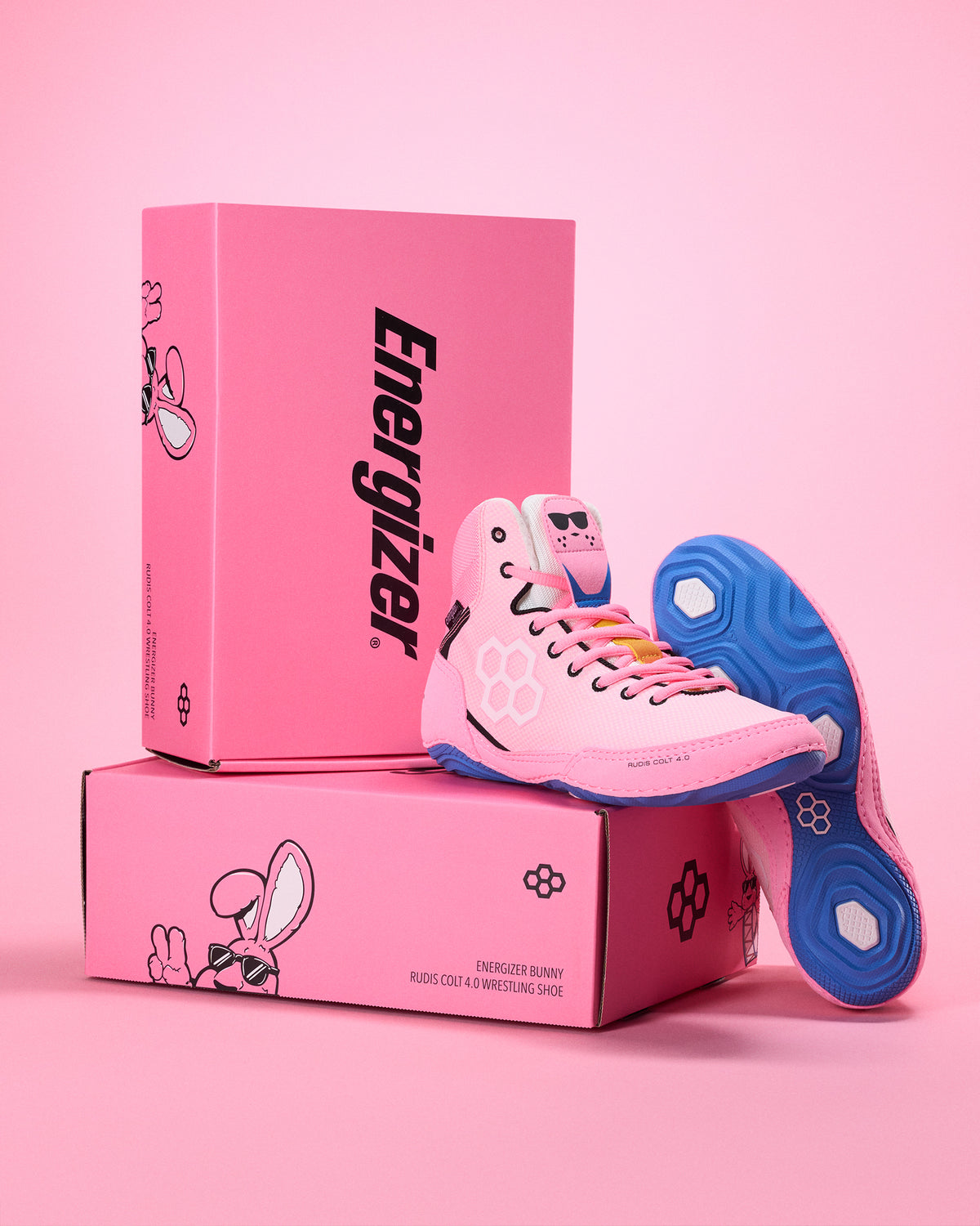 Pink wrestling shoe with blue soles on pink boxes featuring the Energizer logo against a pink background