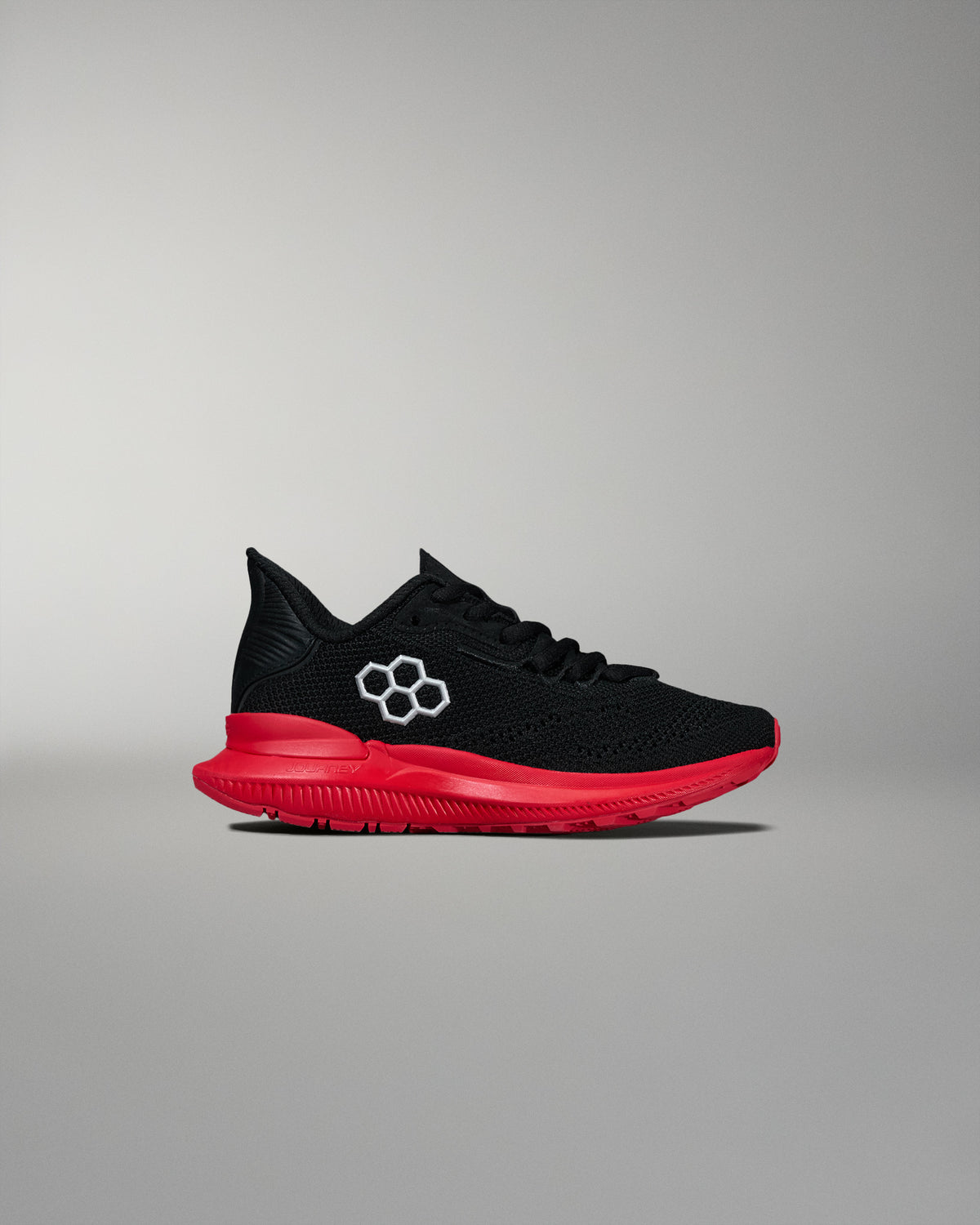 Side view of a black RUDIS training shoe featuring a red midsole and outsole with a white hexagon logo on the upper. Displayed on a neutral gray background.