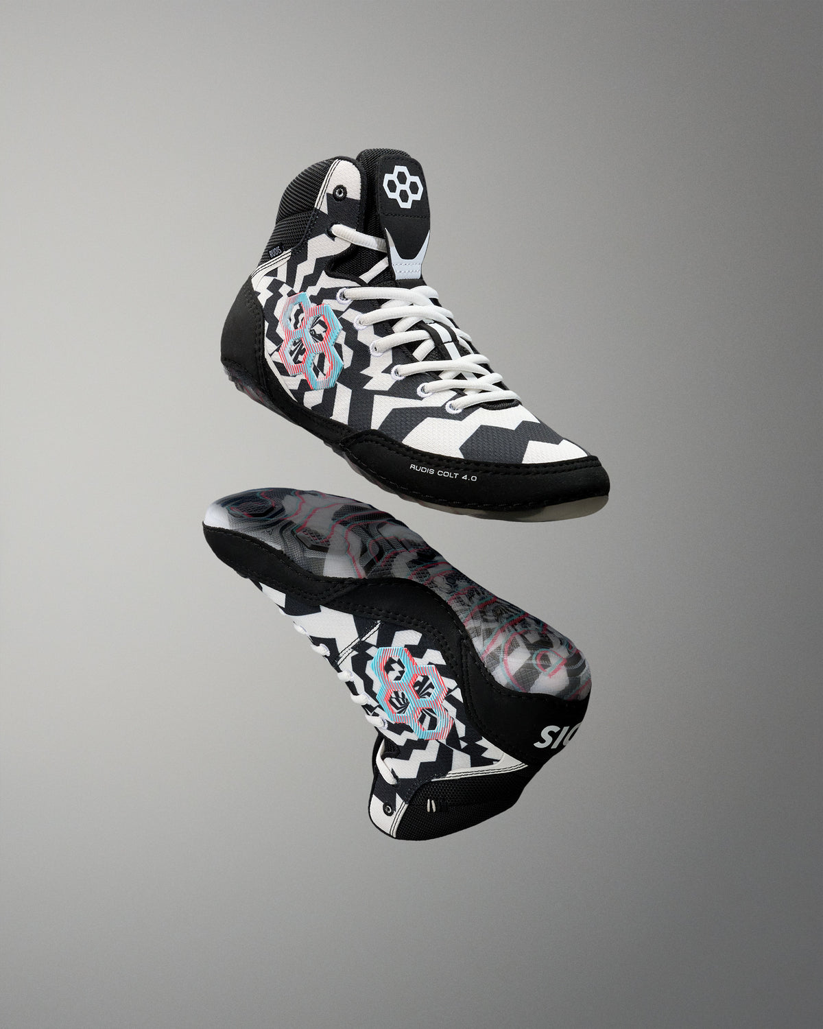A pair of high-top wrestling shoes floating against a neutral gray gradient background. The shoes feature a black, white, and gray geometric pattern with a pink and blue circular graphic on the side and a white logo on the tongue.