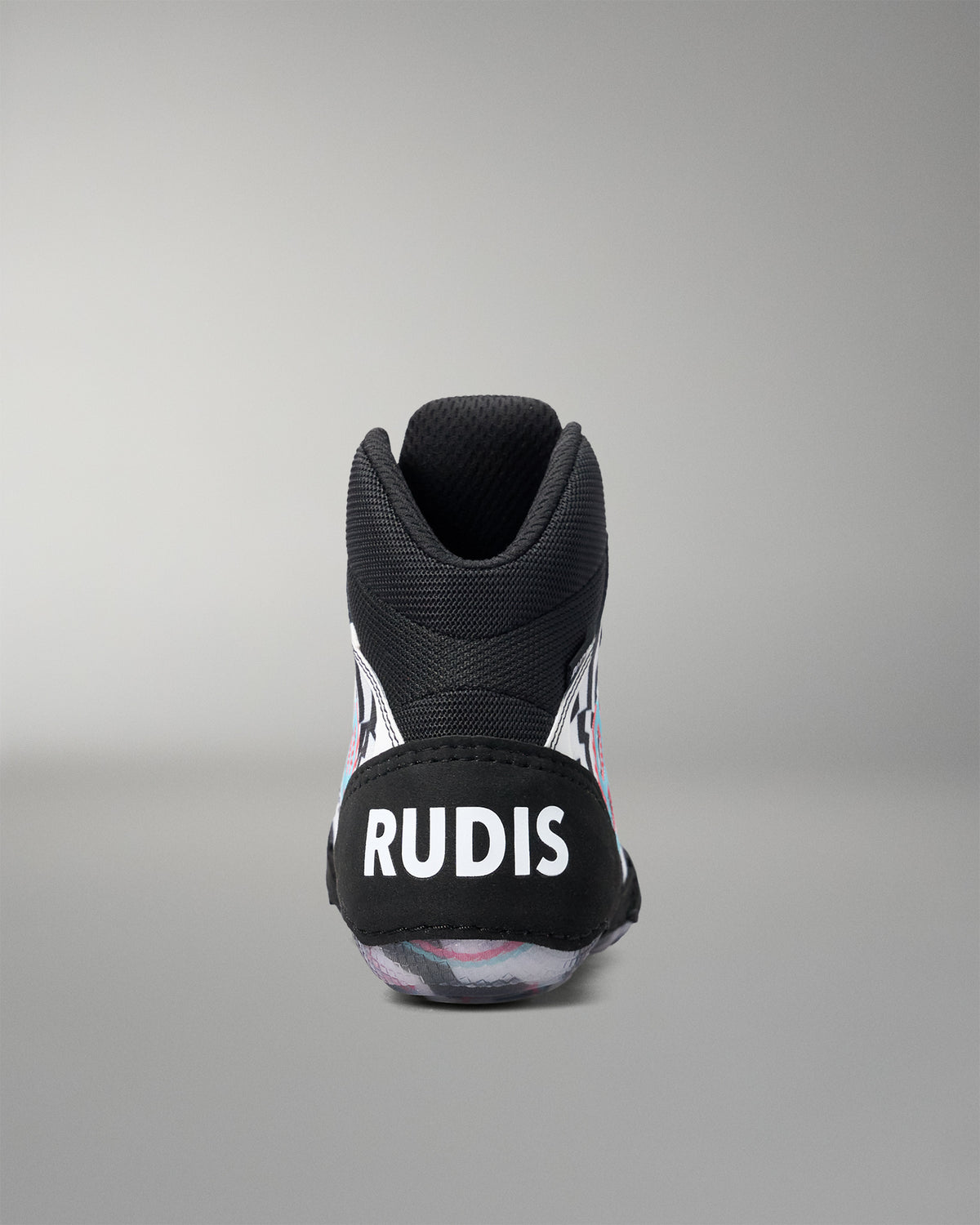 A black high-top wrestling shoe shown from the back, featuring a black heel counter with the brand name 'RUDIS' in bold white letters. The shoe has subtle pink and white graphic details on the sides and a translucent sole.