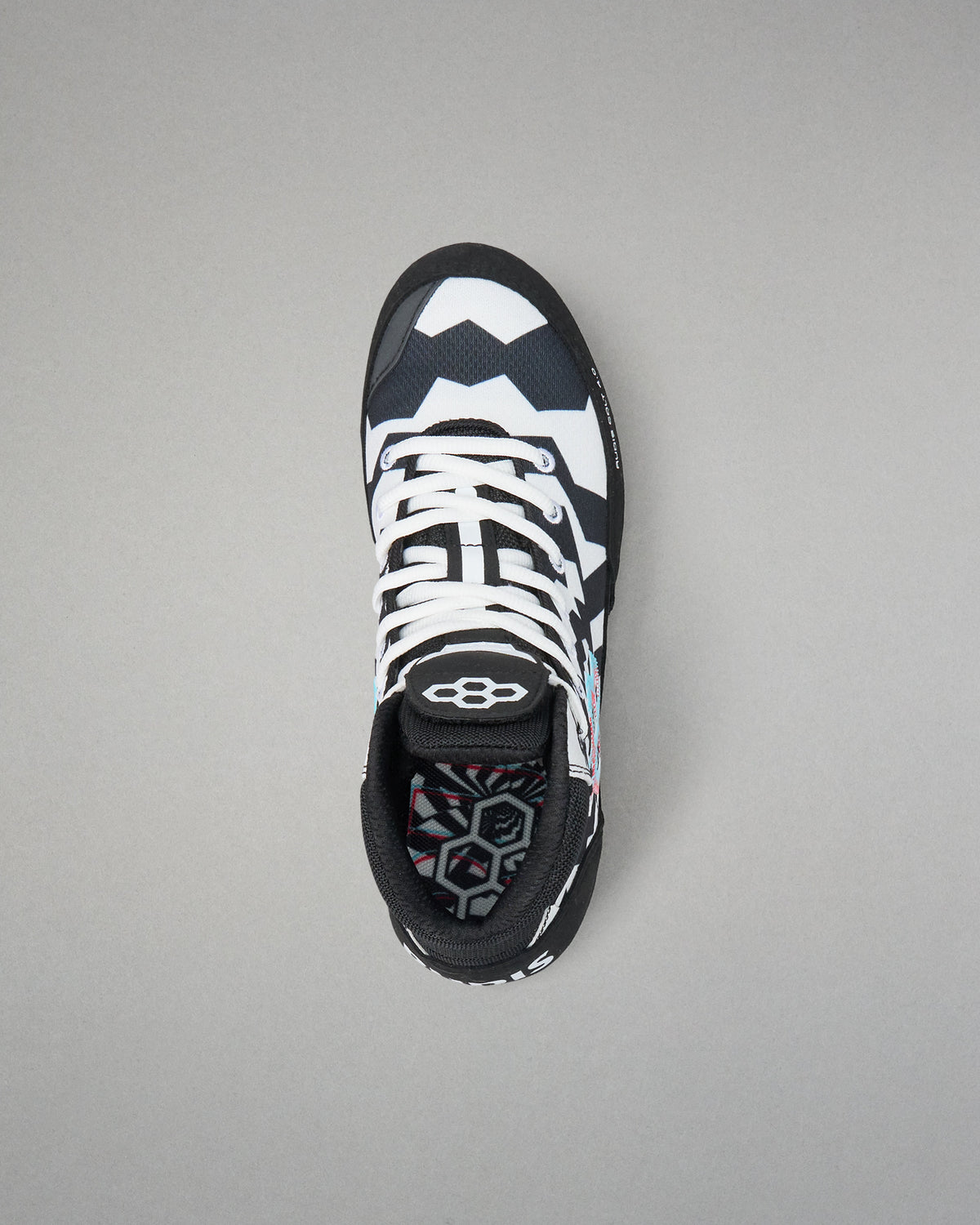 A single high-top wrestling shoe shown from a top-down view on a neutral gray background. The shoe features a black and white geometric pattern on the upper, white laces, and a black collar with a white logo.
