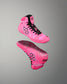 A pair of high-top Wrestling shoes in vibrant pink with black laces, black geometric side logos, and a black heel detail, shown floating against a neutral gray gradient background.