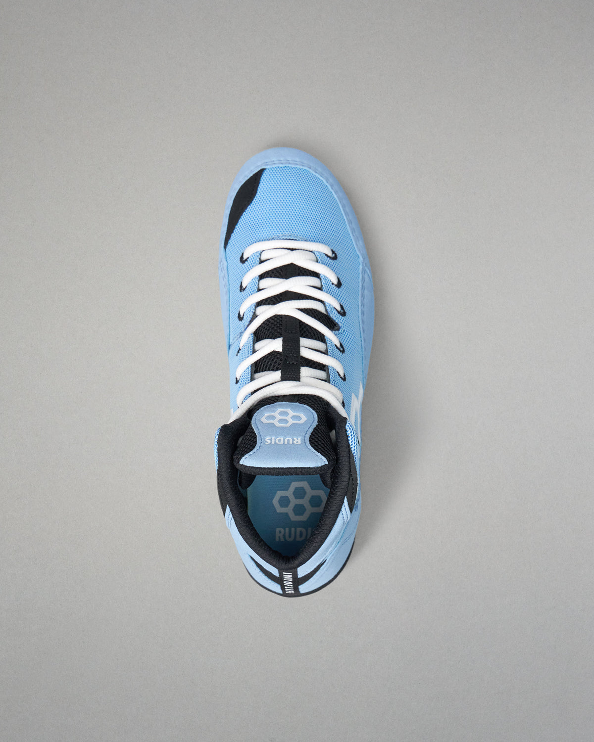 A light blue low-top wrestling shoe with black and white accents, featuring white laces and a visible RUDIS logo on the tongue and heel, photographed from a top-down angle on a neutral gray background.