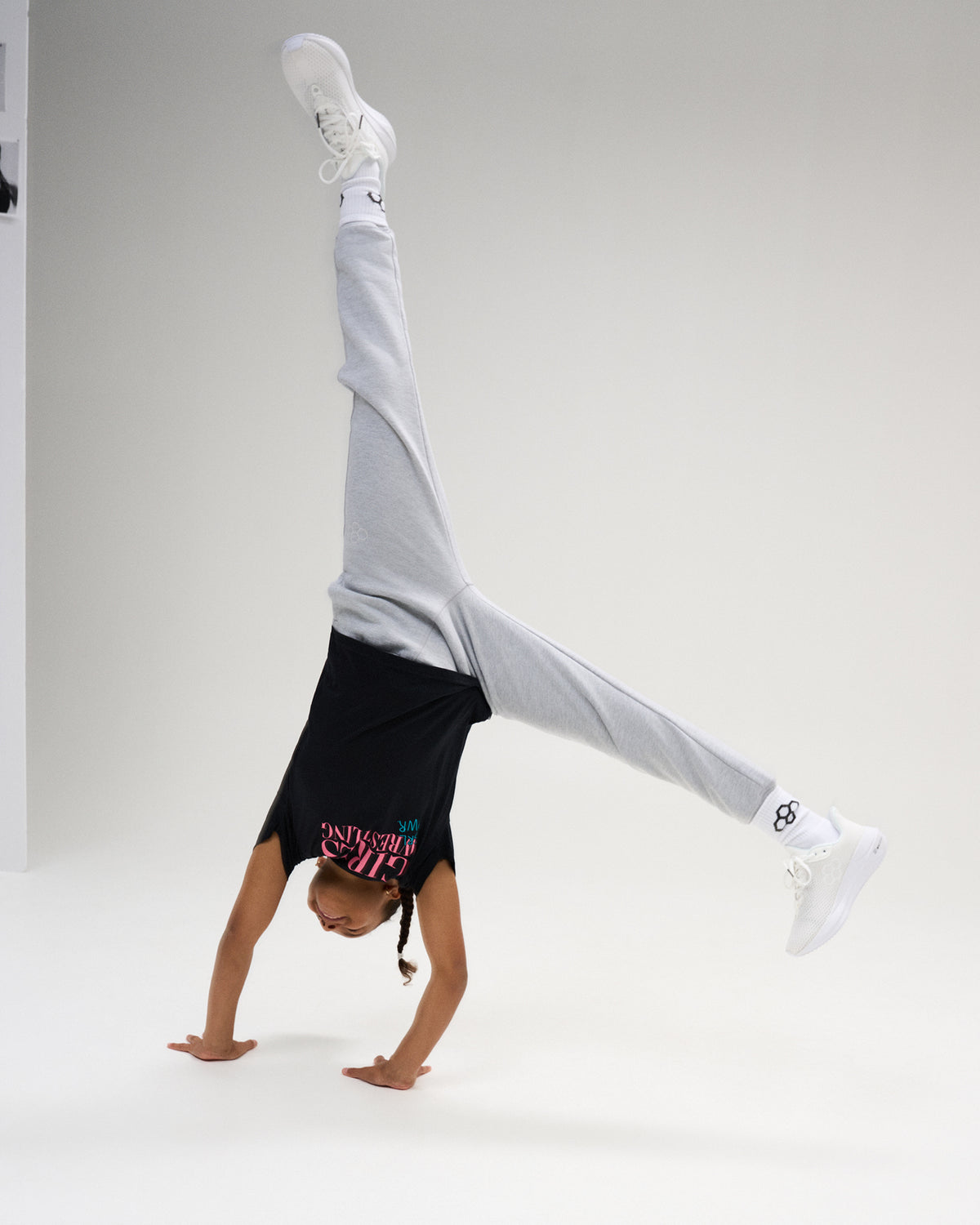 Youth athlete performs a handstand in the black RUDIS Girl Power Wrestling Youth Elite Super Soft T-Shirt with gray joggers and white shoes.