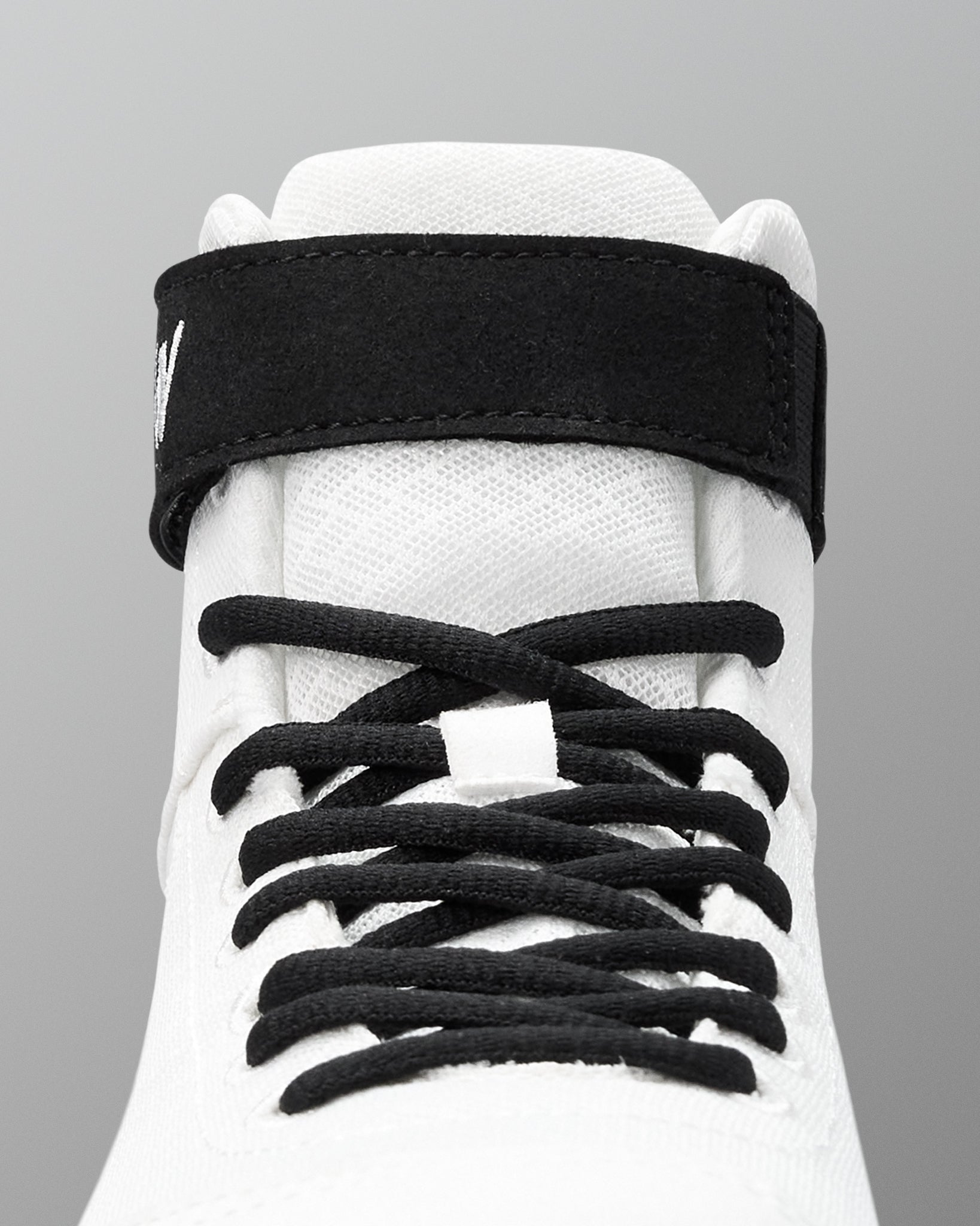 White wrestling shoe with black shoelaces on a gray background