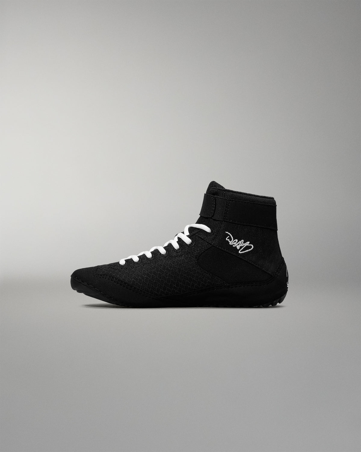 Black wrestling shoe with white laces on a gray background