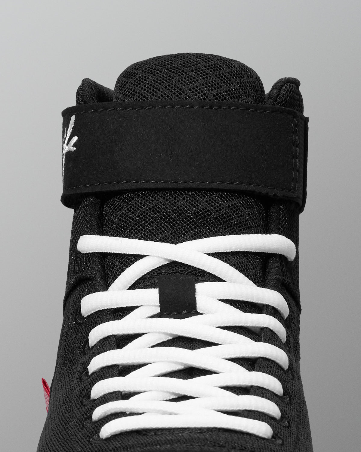 Black wrestling shoe with white laces on a gray background