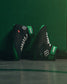 Black and green wrestling shoe with brand logos on a green background