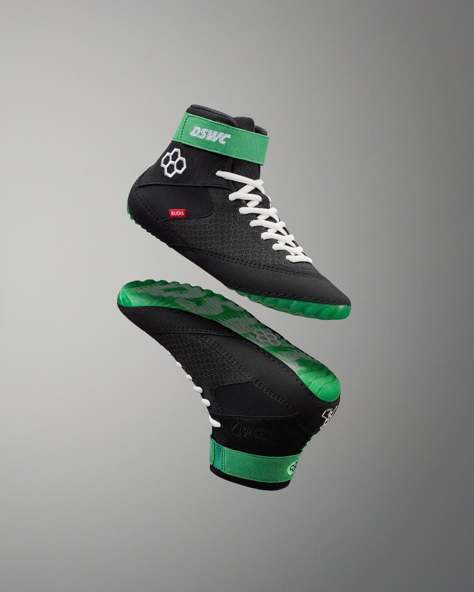 Black and green wrestling shoes with white laces on a gray background