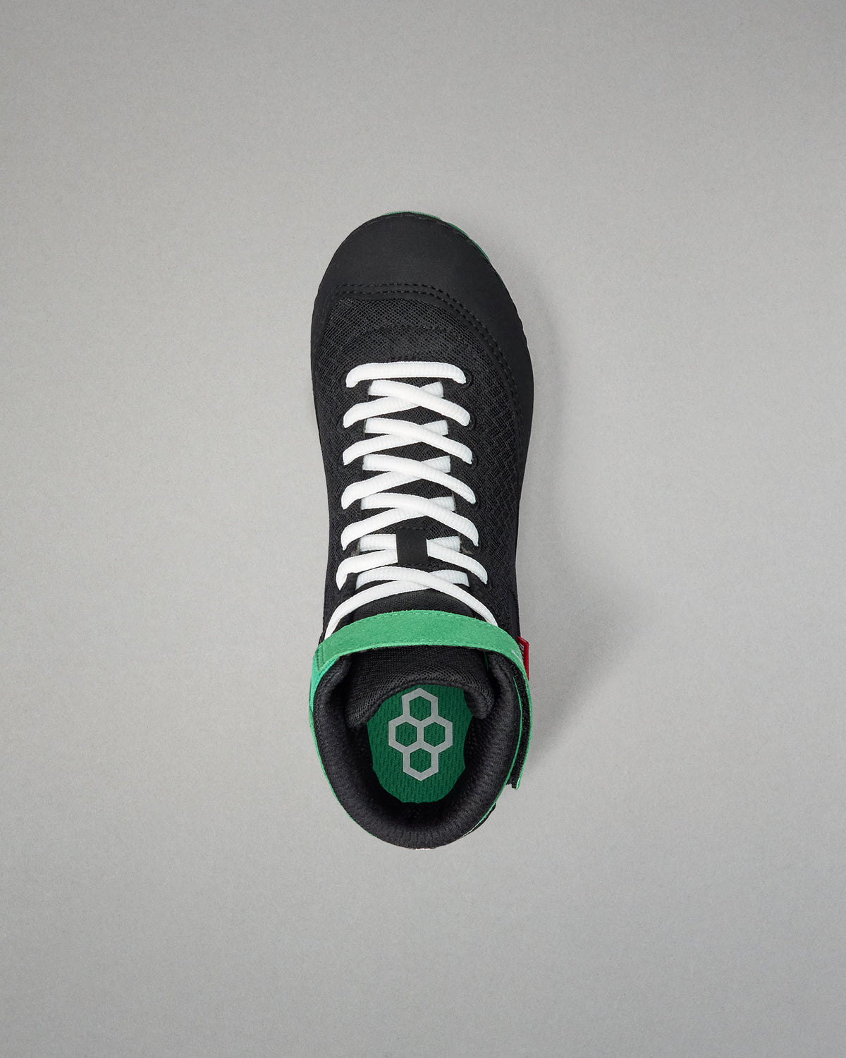 Black wrestling shoe with white laces and green sole on a gray background