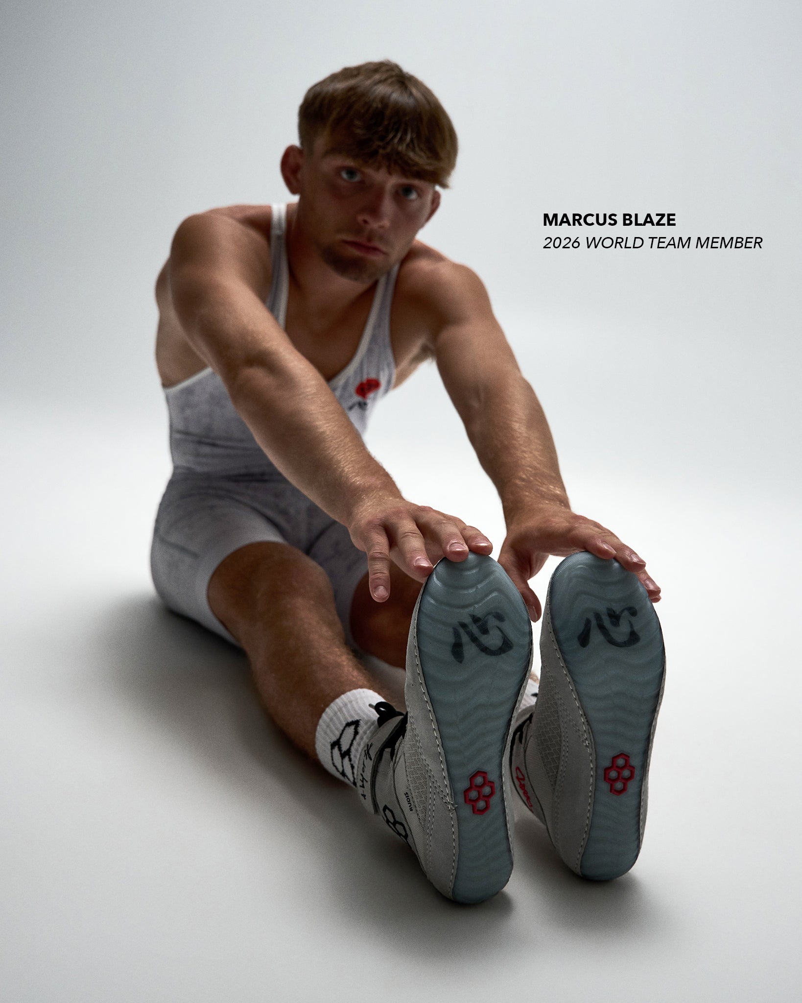 Wrestler, Marcus Blaze, stretching in RUDIS Samurai Speed Youth Wrestling Shoes in Kokoro, showcasing the translucent blue outsoles with red RUDIS emblems and gray high-top design.