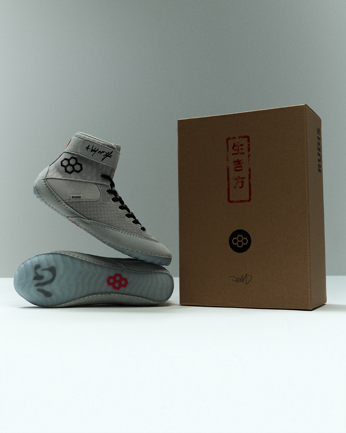 RUDIS Samurai Speed Youth Kokoro wrestling shoes displayed alongside signature RUDIS packaging, featuring gray mesh uppers, black laces, and Japanese-inspired graphics.
