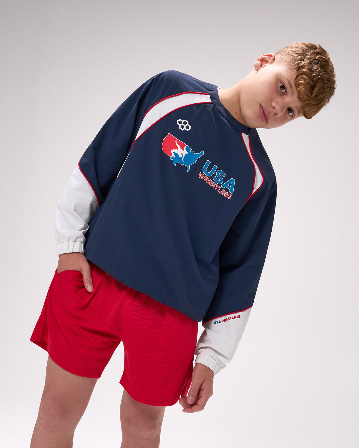 Person wearing a navy sweatshirt with USA Wrestling logo and red shorts on a white background