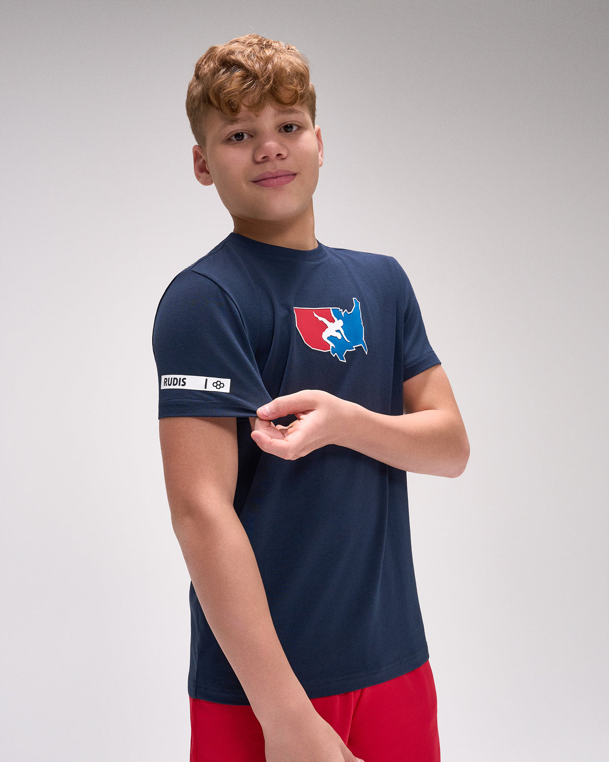 Young boy wearing a navy blue t-shirt with a logo on a gray background