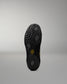 The black sole of a wrestling shoe, shown from a top-down view against a neutral gray background. The sole features a textured pattern of hexagonal and wavy grooves, with a small yellow logo near the center.