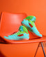 RUDIS Scooby-Doo Colt 4.0 youth wrestling shoes in turquoise and green Mystery Machine colors, displayed on an orange chair with floral graphics and white laces.