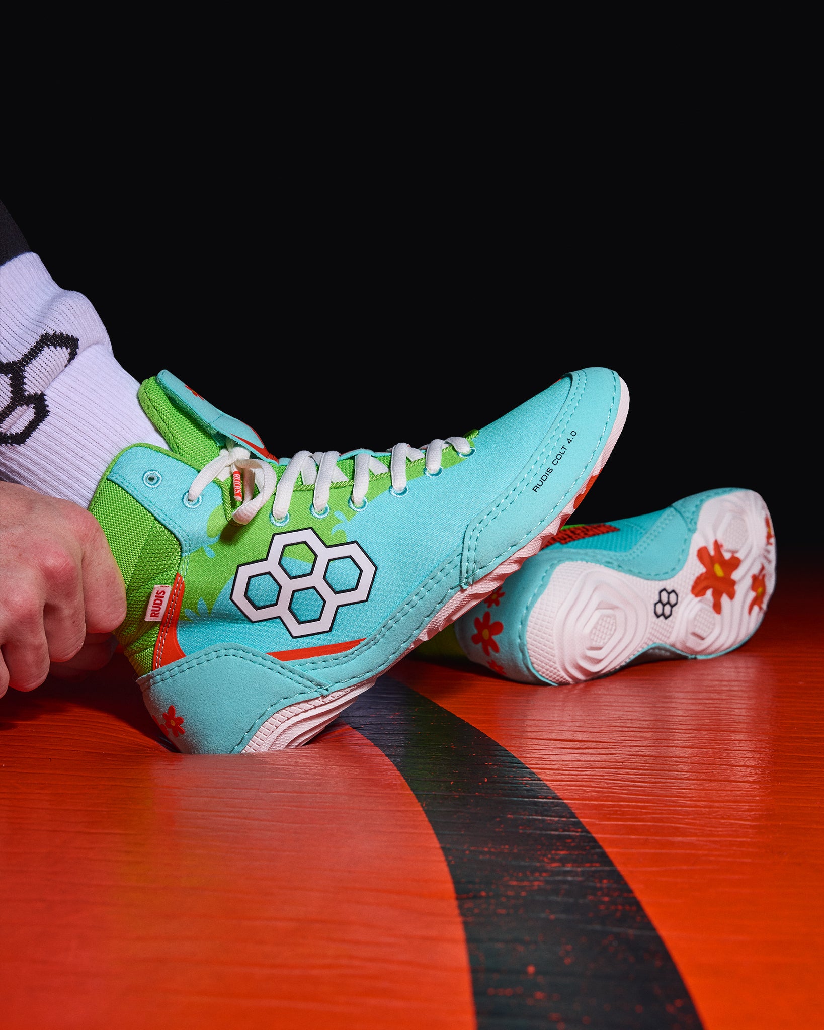 RUDIS Scooby-Doo Colt 4.0 youth wrestling shoes worn on a wrestling mat, highlighting the turquoise upper, green ankle collar, white RUDIS logo, and floral outsole.