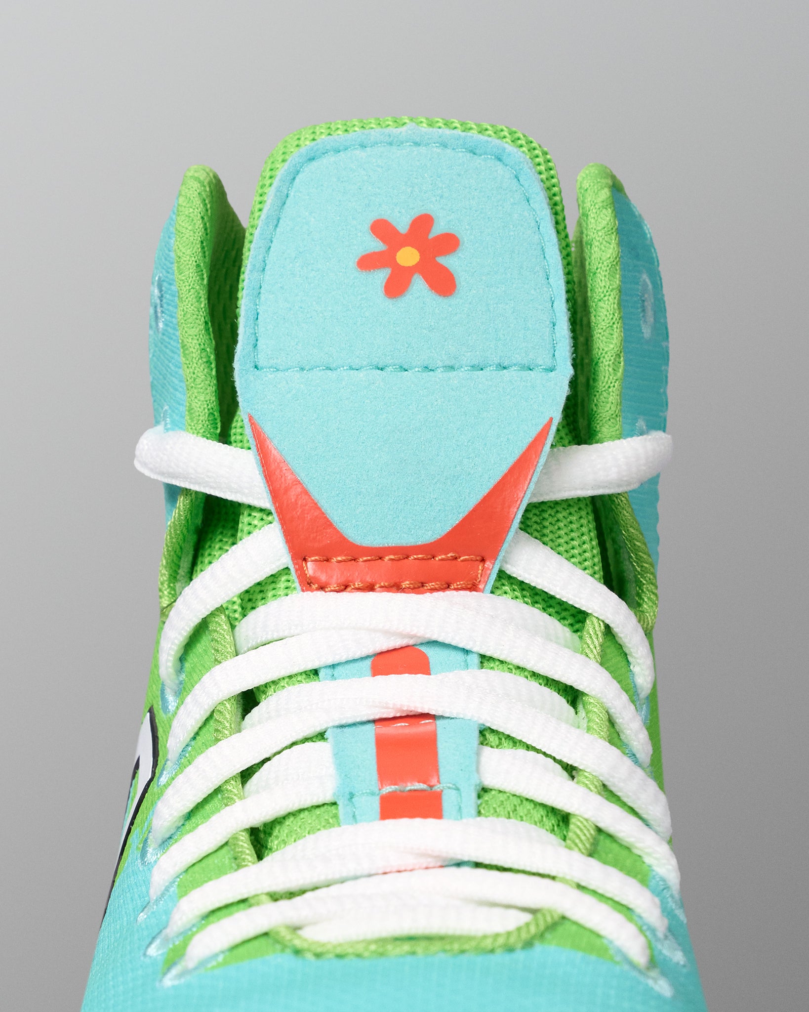 Close-up of the RUDIS Scooby-Doo Colt 4.0 youth wrestling shoe highlighting white laces, green mesh panels, turquoise tongue, and orange flower graphic.